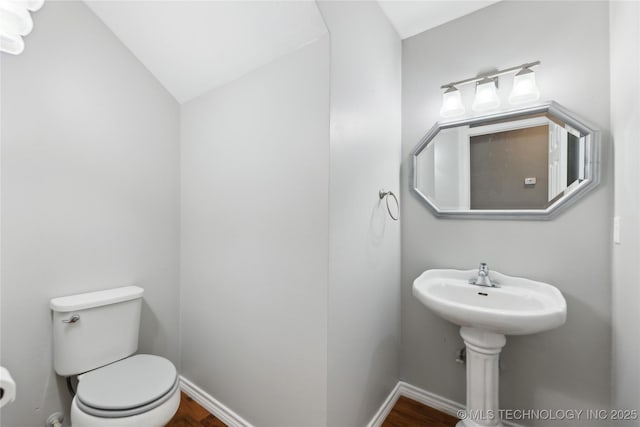 half bathroom with toilet, baseboards, wood finished floors, and lofted ceiling