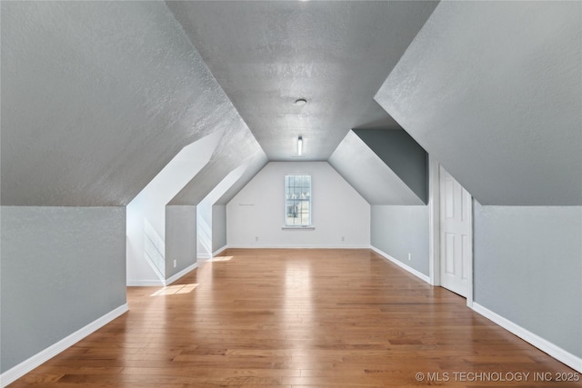 additional living space featuring a textured ceiling, baseboards, lofted ceiling, and hardwood / wood-style floors