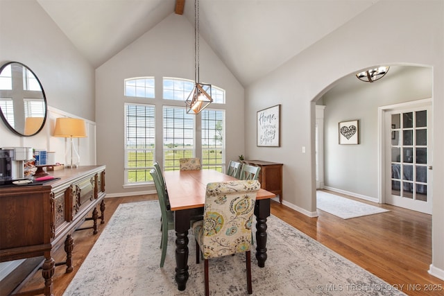 dining space featuring arched walkways, high vaulted ceiling, wood finished floors, and a chandelier