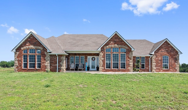 view of front of house with brick siding, roof with shingles, and a front yard