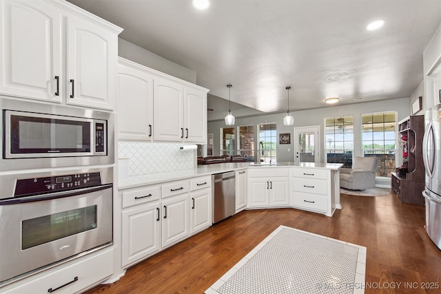 kitchen with dark wood-style flooring, stainless steel appliances, recessed lighting, a peninsula, and backsplash