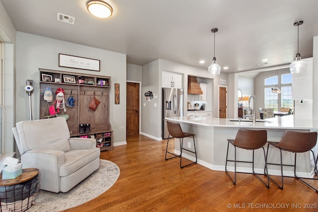 kitchen featuring a breakfast bar area, stainless steel refrigerator with ice dispenser, visible vents, a sink, and light countertops