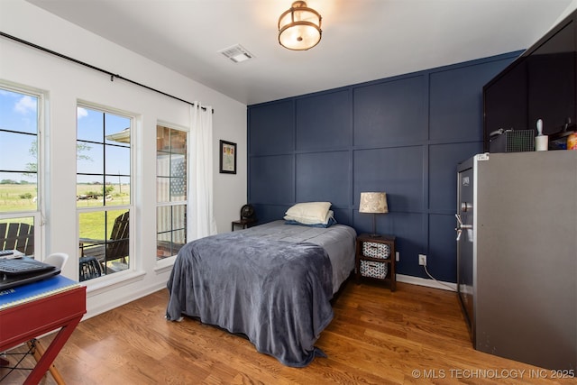bedroom with access to outside, visible vents, wood finished floors, and a decorative wall