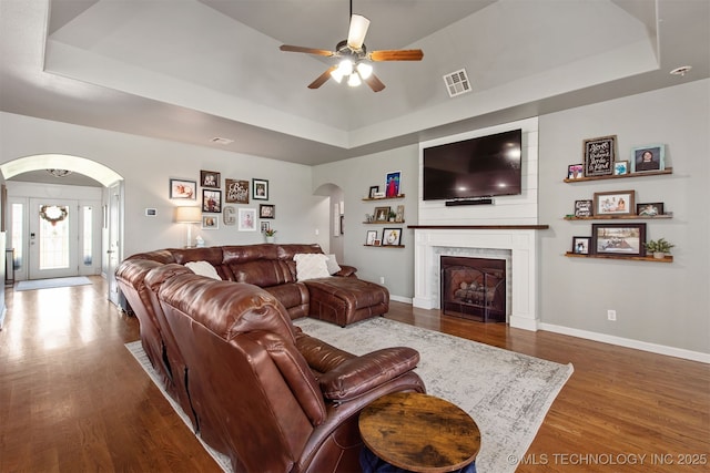living room featuring ceiling fan, visible vents, arched walkways, wood finished floors, and a raised ceiling