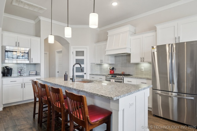 kitchen with tasteful backsplash, appliances with stainless steel finishes, a sink, visible vents, and premium range hood
