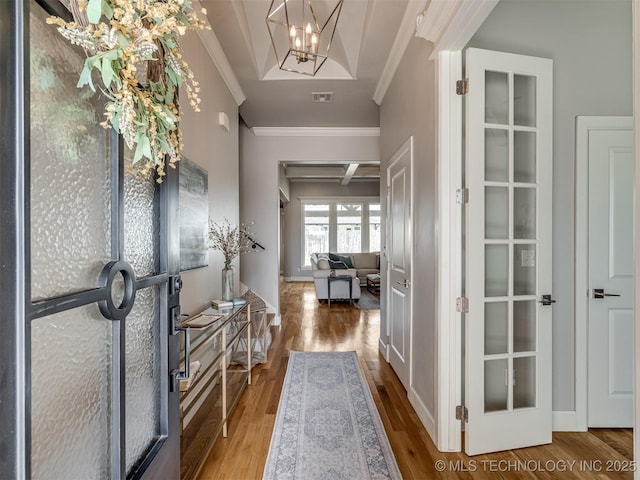 foyer featuring visible vents, wood finished floors, ornamental molding, and a chandelier