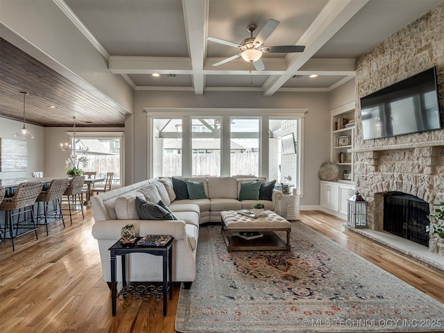 living area with coffered ceiling, a stone fireplace, light wood-type flooring, ceiling fan with notable chandelier, and beamed ceiling