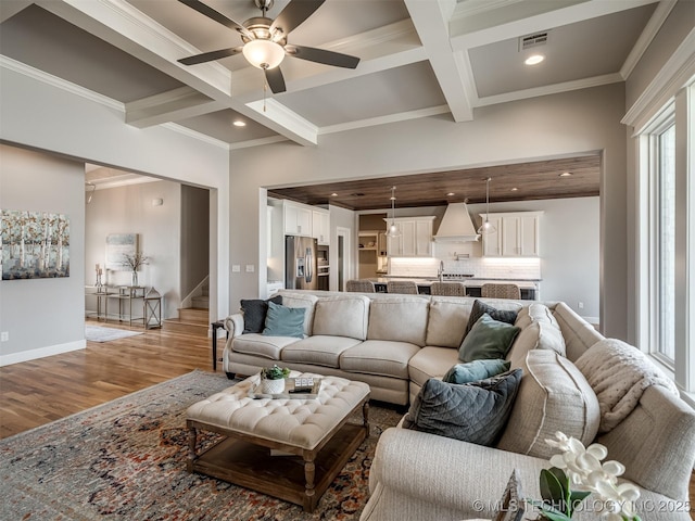 living area with beamed ceiling, stairs, wood finished floors, a ceiling fan, and coffered ceiling