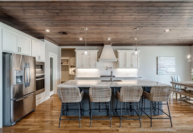 kitchen with wooden ceiling, wood finished floors, stainless steel appliances, and premium range hood