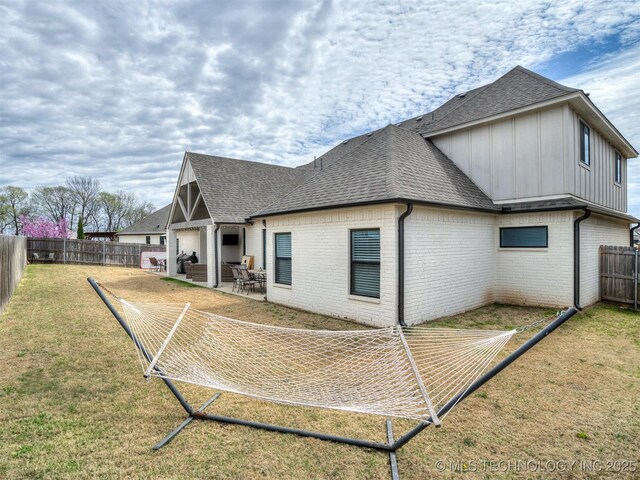 rear view of house with a fenced backyard, brick siding, a shingled roof, a yard, and a patio area