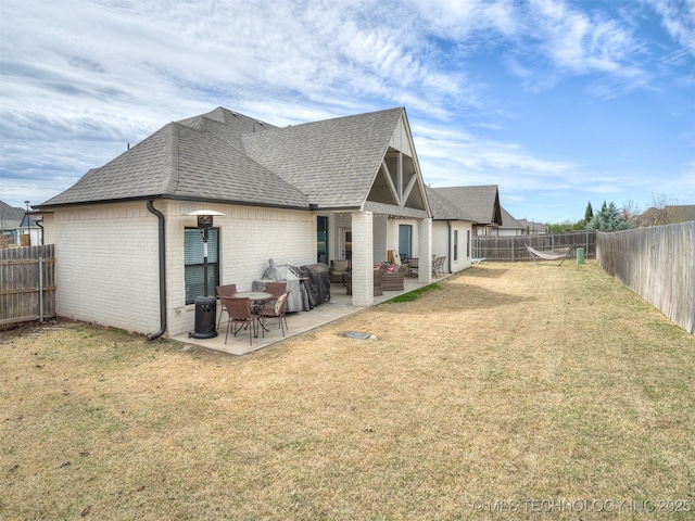 back of property featuring roof with shingles, a patio, a fenced backyard, brick siding, and a lawn