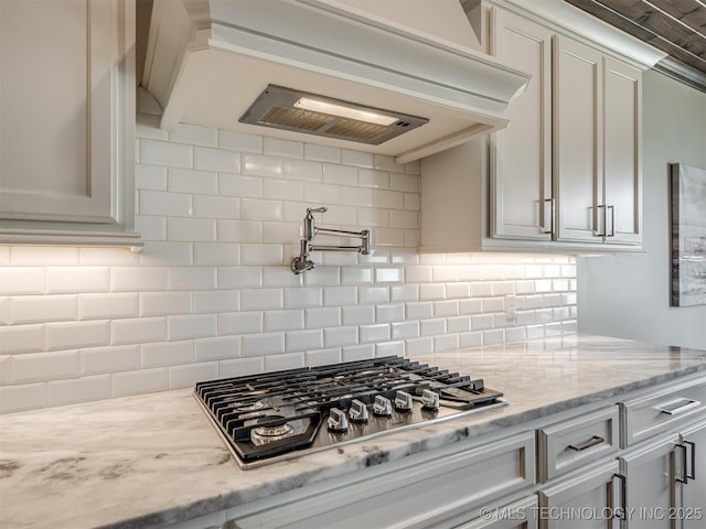 kitchen with stainless steel gas cooktop, backsplash, light stone countertops, custom range hood, and white cabinets