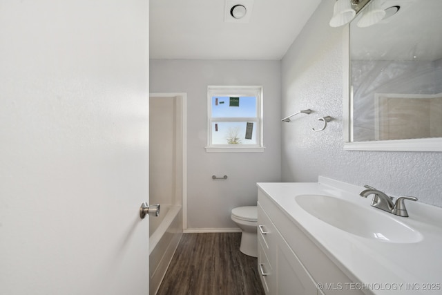 bathroom with vanity, toilet, a textured wall, baseboards, and wood finished floors