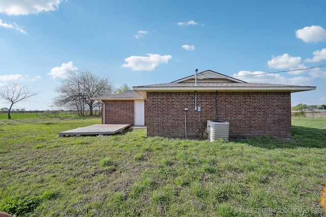 view of home's exterior with brick siding, central AC unit, a deck, and a lawn