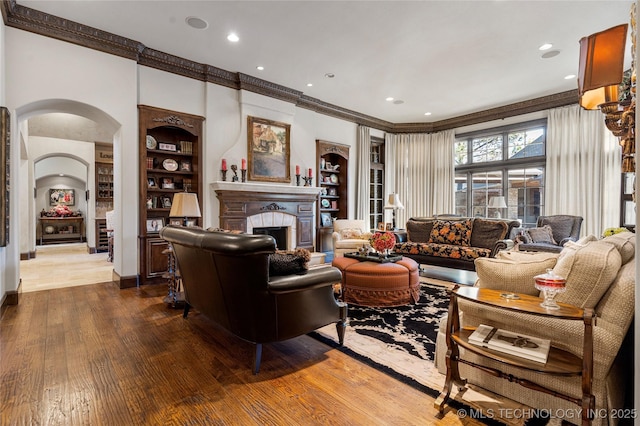 living area with recessed lighting, dark wood finished floors, arched walkways, crown molding, and a fireplace