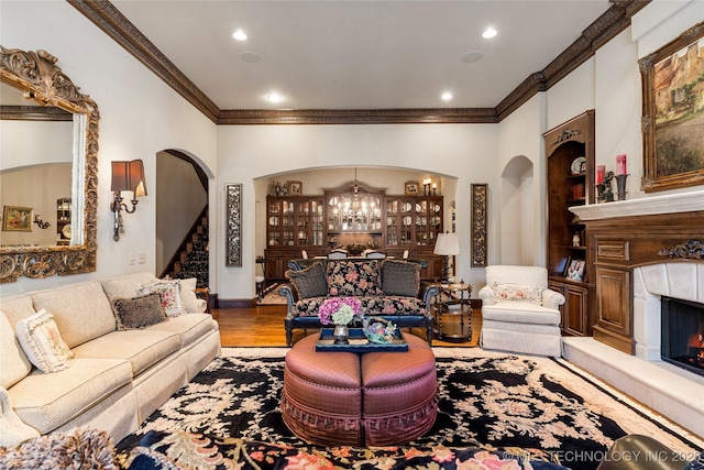 living area featuring stairway, an inviting chandelier, a warm lit fireplace, ornamental molding, and arched walkways