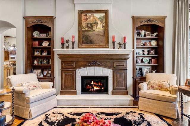sitting room featuring arched walkways, built in features, wood finished floors, and a warm lit fireplace