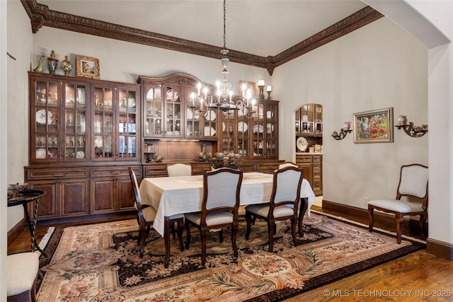 dining room featuring wood finished floors, a chandelier, arched walkways, baseboards, and ornamental molding