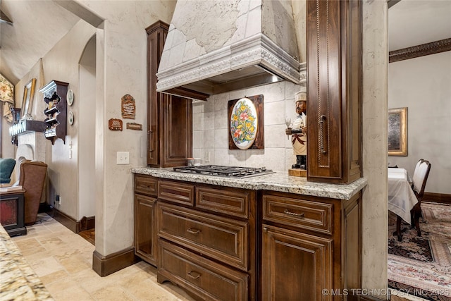 bar with stone tile flooring, baseboards, stainless steel gas cooktop, tasteful backsplash, and custom exhaust hood