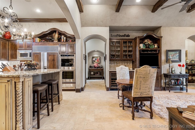 wine room featuring ceiling fan with notable chandelier, arched walkways, a towering ceiling, beamed ceiling, and wine cooler