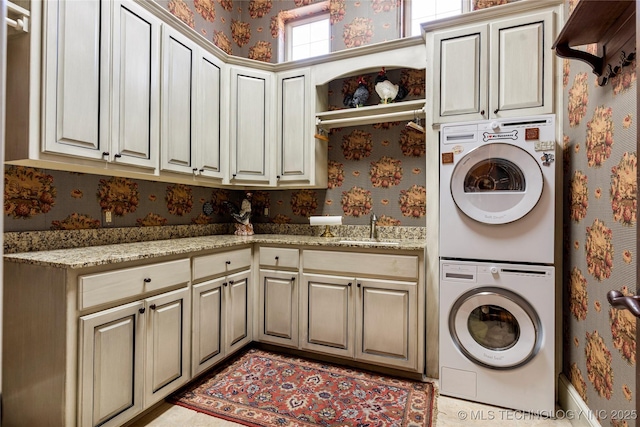 washroom featuring cabinet space, wallpapered walls, stacked washer / dryer, and a sink