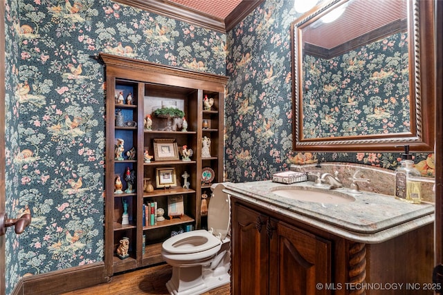 bathroom with wood finished floors, wallpapered walls, vanity, toilet, and ornamental molding