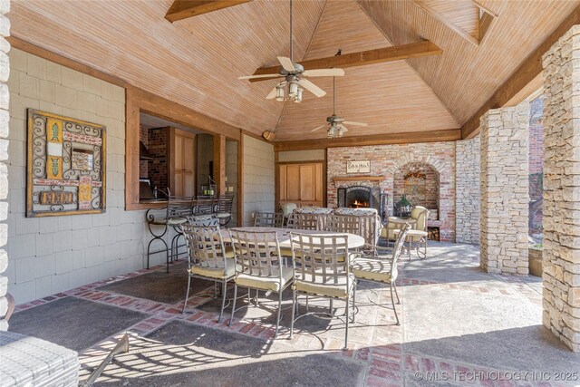 view of patio / terrace featuring a warm lit fireplace, a ceiling fan, and outdoor dining space