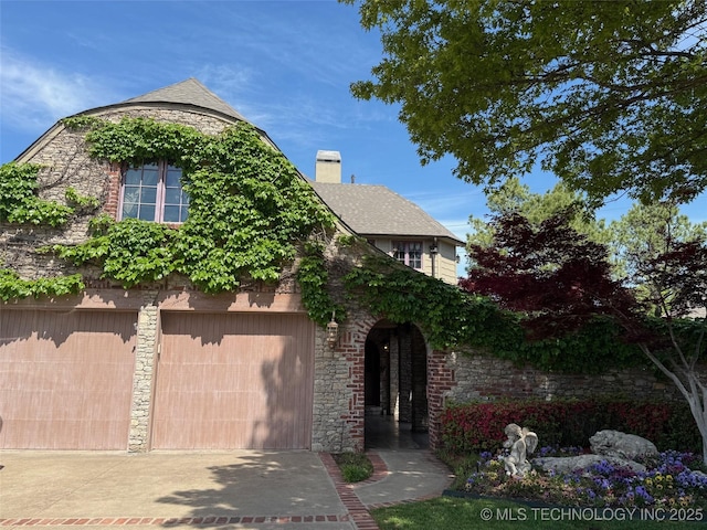 view of front of home featuring driveway, stone siding, an attached garage, and a chimney