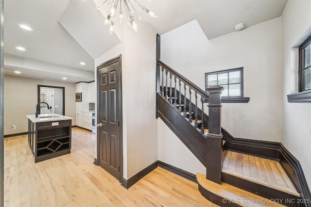 staircase featuring a notable chandelier, hardwood / wood-style flooring, baseboards, and recessed lighting