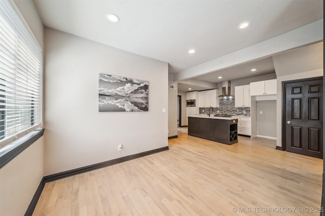 kitchen with light countertops, backsplash, light wood-type flooring, wall chimney range hood, and white cabinets