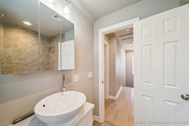 bathroom featuring a sink, baseboards, visible vents, and tiled shower