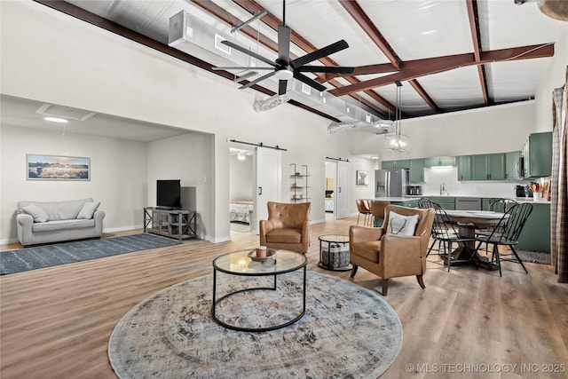 living area with light wood-type flooring, baseboards, a barn door, beamed ceiling, and ceiling fan