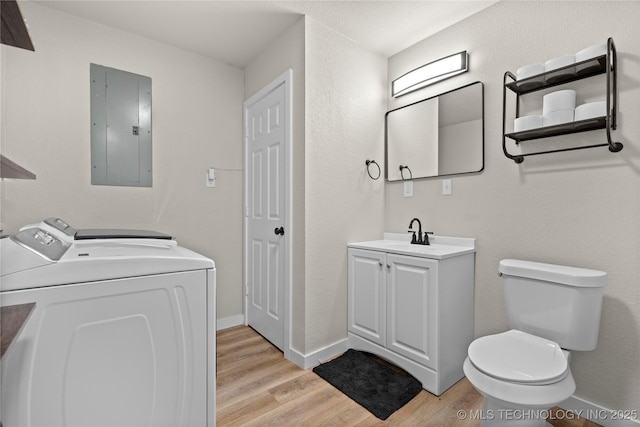 bathroom with electric panel, washing machine and dryer, toilet, wood finished floors, and baseboards