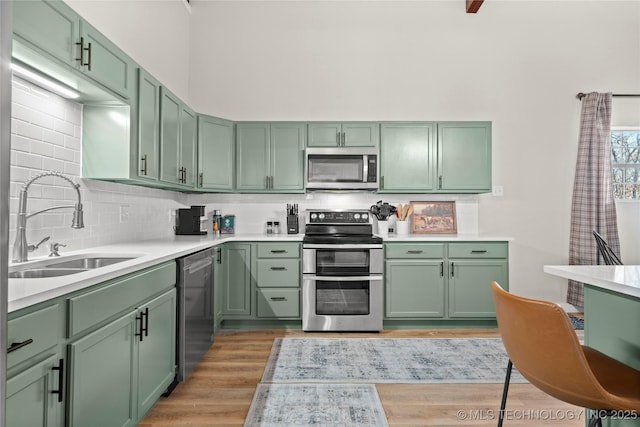 kitchen with green cabinets, light wood-type flooring, appliances with stainless steel finishes, and a sink