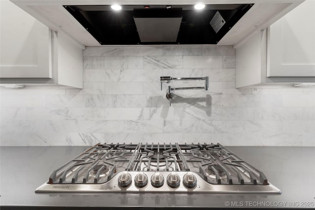 interior details featuring tasteful backsplash, extractor fan, stainless steel gas cooktop, and white cabinetry