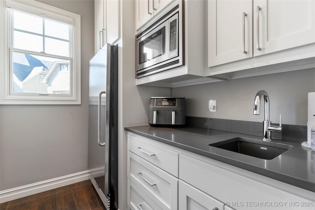 kitchen with dark countertops, white cabinetry, a sink, and appliances with stainless steel finishes