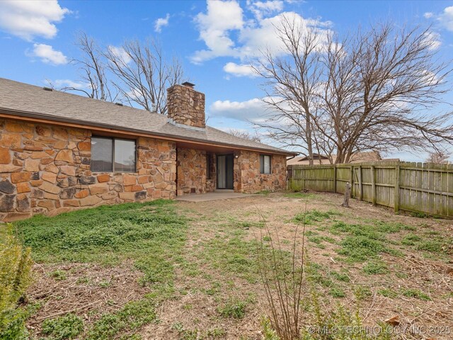 rear view of house with stone siding, a chimney, fence, and a patio area