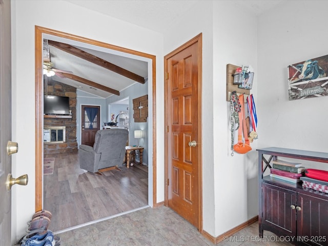 foyer featuring a ceiling fan, vaulted ceiling with beams, a fireplace, wood finished floors, and baseboards