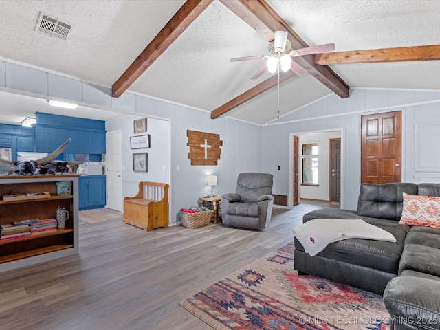 living area with lofted ceiling with beams, a textured ceiling, visible vents, ceiling fan, and wood finished floors