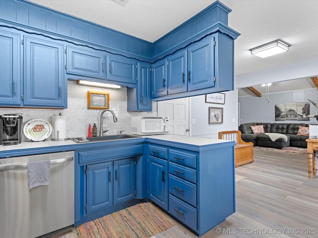 kitchen with blue cabinetry, a sink, white microwave, and stainless steel dishwasher