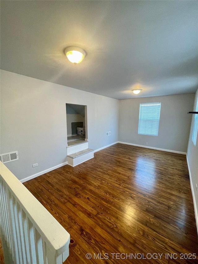 unfurnished living room featuring dark wood-style flooring, baseboards, and visible vents