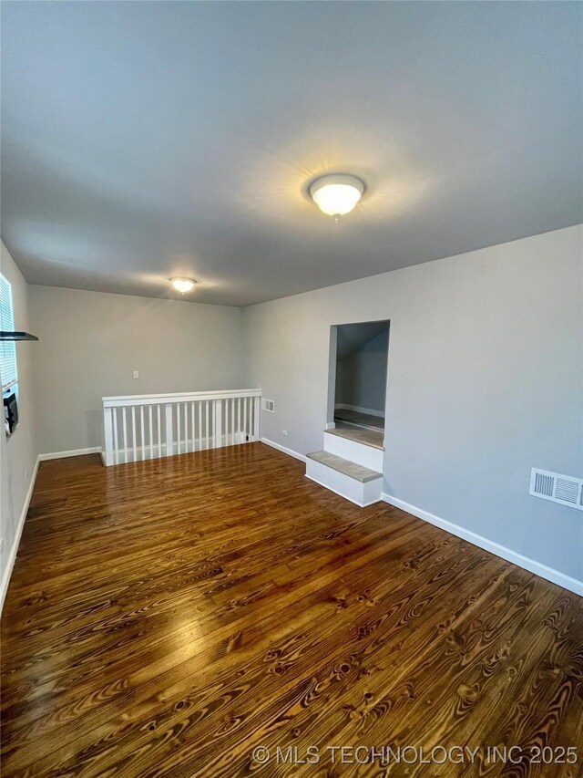 unfurnished room with dark wood-style floors, visible vents, baseboards, and a glass covered fireplace