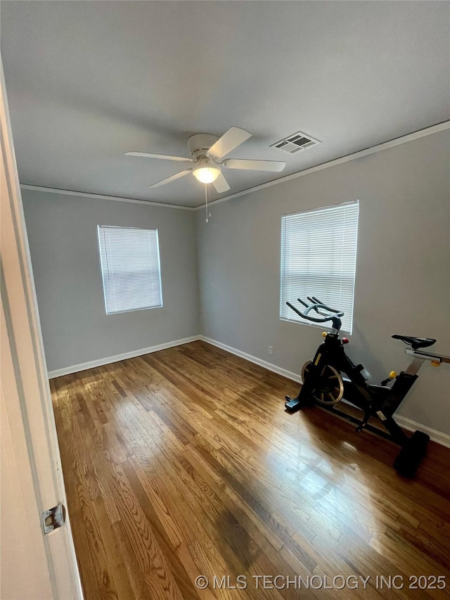 spare room featuring visible vents, baseboards, ornamental molding, wood finished floors, and a ceiling fan