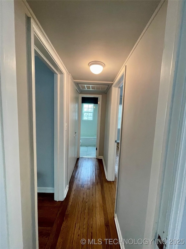 hall with dark wood finished floors, baseboards, visible vents, and ornamental molding