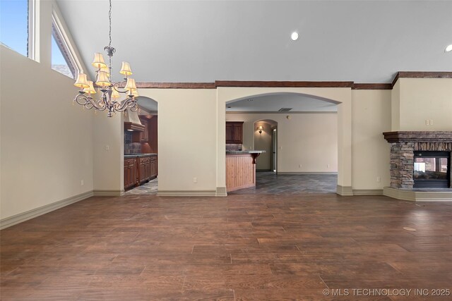 9707 E 90th Ct N, Owasso, OK 74055 - unfurnished living room with crown molding, baseboards, arched walkways, dark wood-style floors, and an inviting chandelier