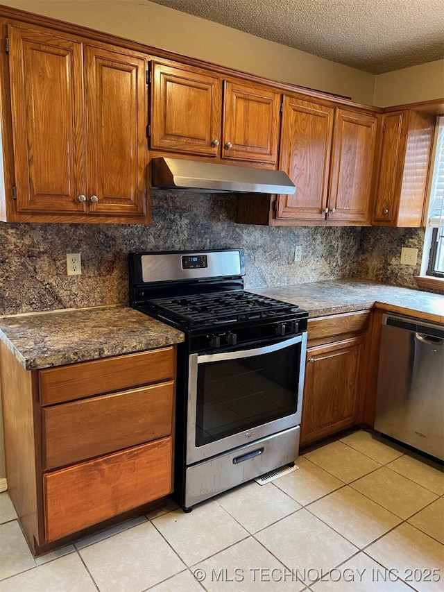 kitchen featuring light tile patterned flooring, under cabinet range hood, brown cabinets, and stainless steel appliances
