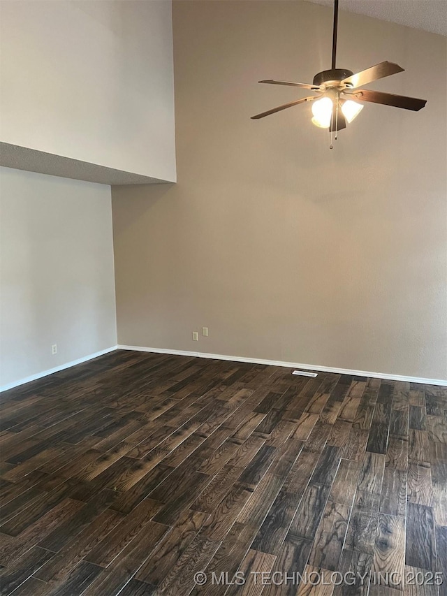 empty room featuring baseboards, dark wood-style flooring, high vaulted ceiling, and a ceiling fan
