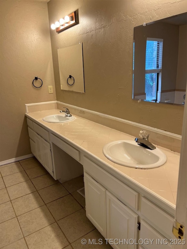 bathroom featuring double vanity, a sink, a textured wall, and tile patterned flooring
