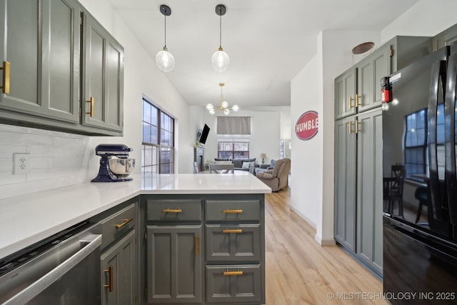 kitchen featuring backsplash, stainless steel dishwasher, freestanding refrigerator, a peninsula, and an inviting chandelier
