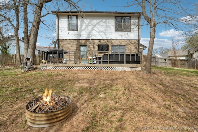 rear view of property featuring a fire pit, a wooden deck, fence, brick siding, and a lawn